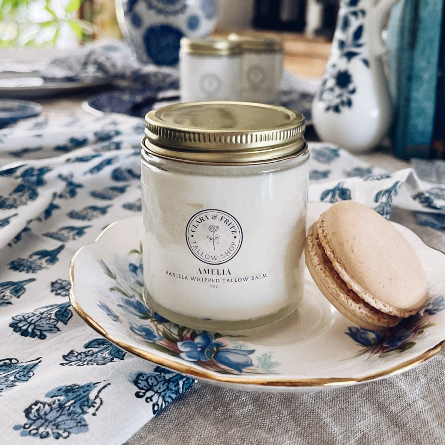 Amelia Vanilla Whipped Tallow Balm on decorative plate with macaron, nourishing skin moisturizer in glass jar.