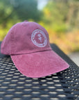 Garment-Washed Logo Hat in burgundy with Clara & Fritz emblem on a picnic table, showcasing its stylish and comfortable design for sunny days.