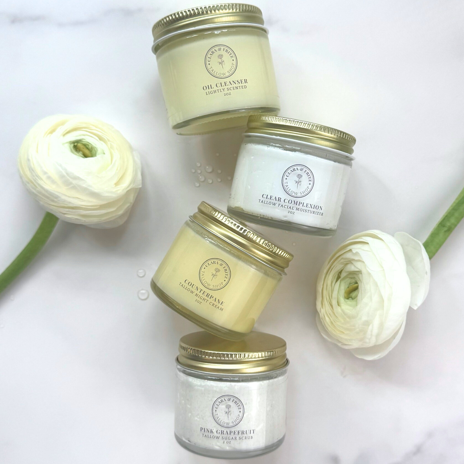 Alt Tag: Capsule Skincare Kit featuring four luxurious facial products with elegant jar packaging surrounded by white flowers.