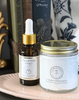 Bottle of Clara & Fritz serum and jar of moisturizer on a plate with books in the background