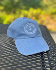 Garment-Washed Logo Hat in periwinkle with Clara & Fritz logo on a textured surface, perfect for sunny days and casual wear.