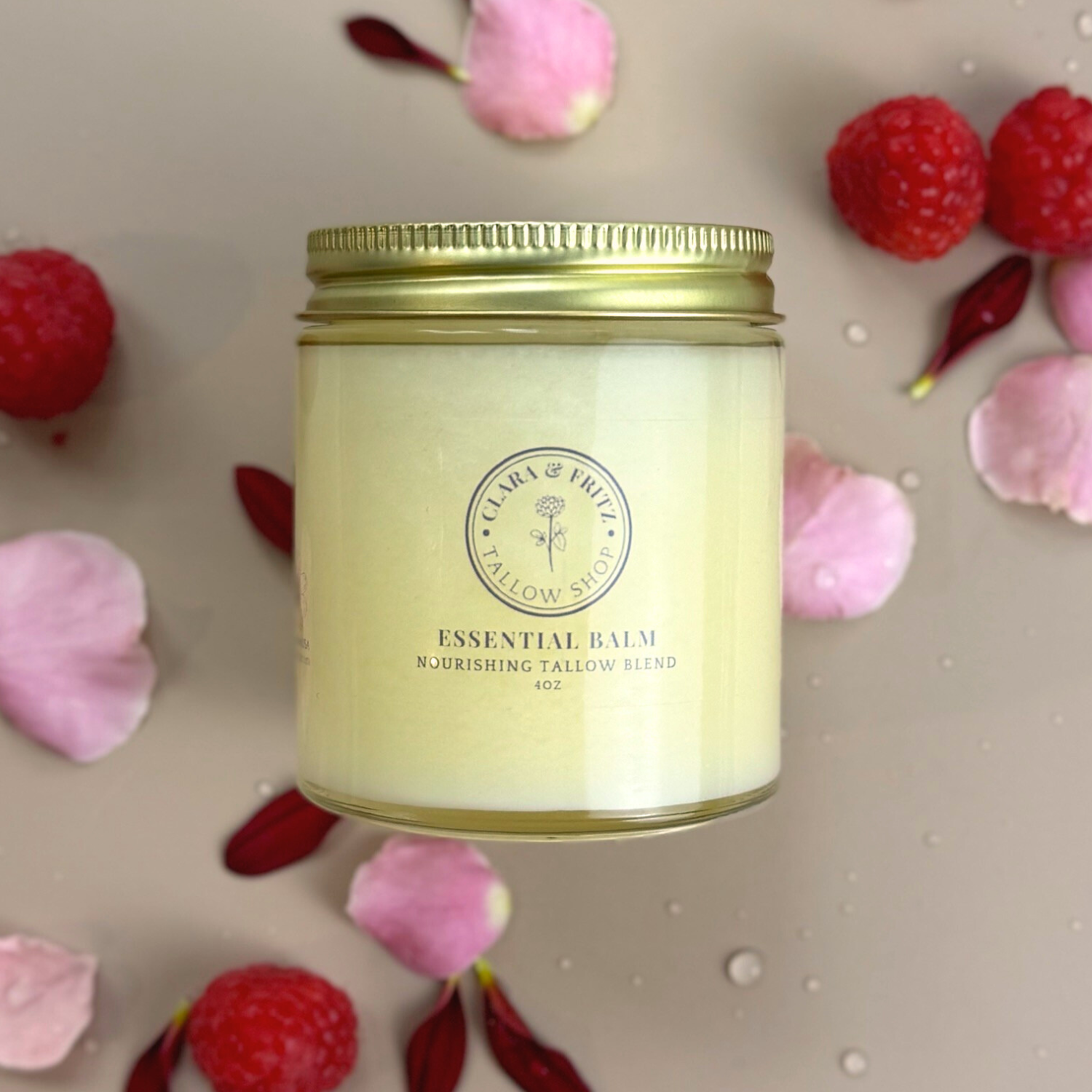 Essential Balm with Infused Calendula in a glass jar surrounded by pink petals and red berries on a beige surface.