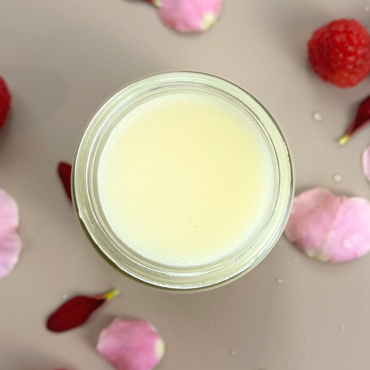 Essential Balm with Infused Calendula in a jar surrounded by petals and raspberries, ideal for natural skincare.