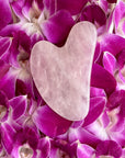 Rose Quartz Gua Sha Tool resting on vibrant purple flower petals, designed for skincare to enhance radiance and circulation.