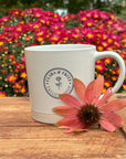 Latte Mug featuring Clara & Fritz logo with pink flower, perfect for coffee lovers, gift idea for loved ones, set against vibrant flowers