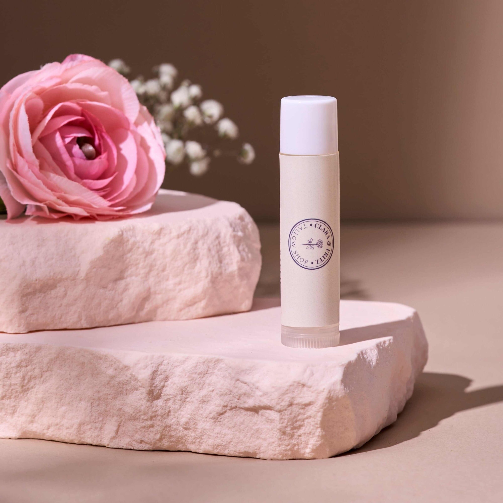 Tallow Lip Balm - Single displayed with pink rose and stone background for moisturizing lip care. Also included in Lip Balm Set.
