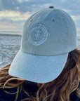 Garment-Washed Logo Hat in Blue on woman at beach, featuring Clara & Fritz logo, made from cotton twill, ideal for sunny days. Stylish and comfortable.