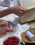 Coastal Rattan Tray used in a picnic setting with book, raspberries, grapefruit, and skincare items displayed stylishly.