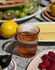 Garden Rose Juice Glass with fruit and butter on a dining table, showcasing elegant ribbed design.