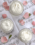 Seasonal Scent Gift Set balm in glass jars on sheet music with rose petals, showcasing its luxurious texture.
