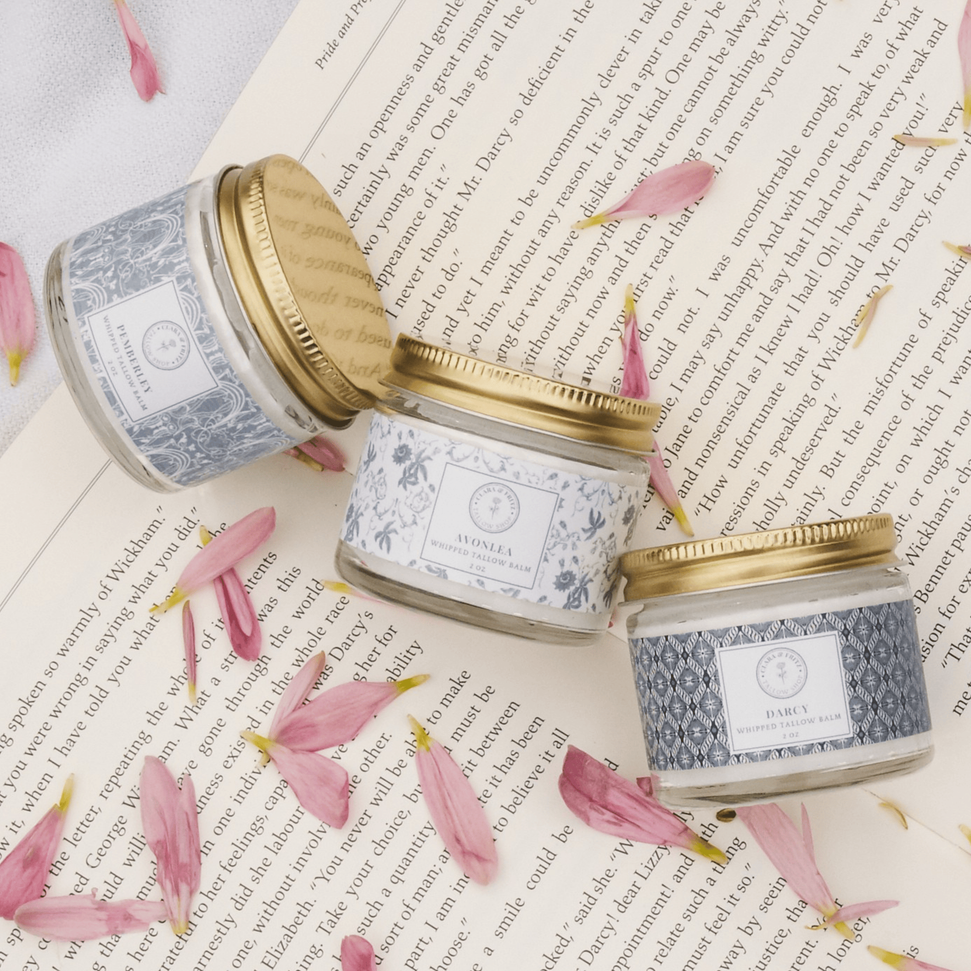 Signature Scent Trio Whipped Moisturizer Set with floral jars displayed on an open book, surrounded by pink petals.