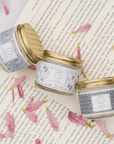 Signature Scent Trio Whipped Moisturizer Set with floral jars displayed on an open book, surrounded by pink petals.
