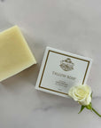 Unscented tallow soap bar displayed with packaging and white rose on marble surface.