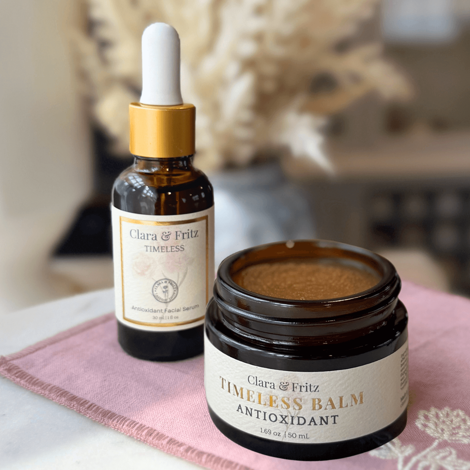 Timeless Serum and Antioxidant Balm Set displayed on a pink cloth, showcasing skincare products for radiant, resilient skin.