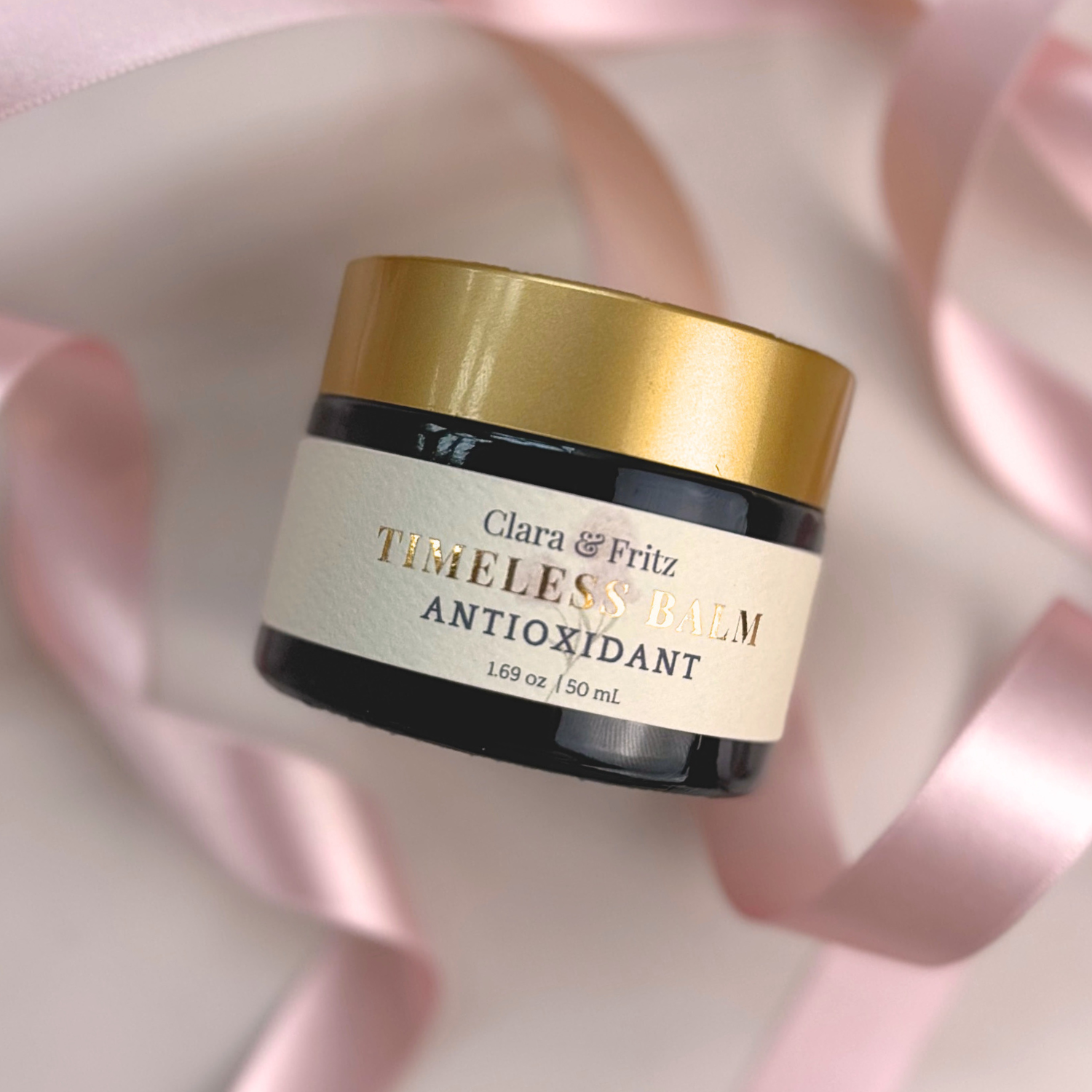 Jar of Timeless Antioxidant Balm with gold lid surrounded by pink ribbon.