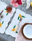 Elegant table setting with rattan placemats, white quilted napkins with lemon designs, pink roses, and a Coastal Rattan Tray.