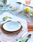 Table setting featuring the Coastal Rattan Tray with white dishes and Garden Rose Juice Glass, surrounded by lemons and floral decor.