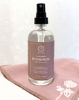 Lavender Hydrosol spray bottle for facial use, displayed on a pink cloth with floral embroidery.