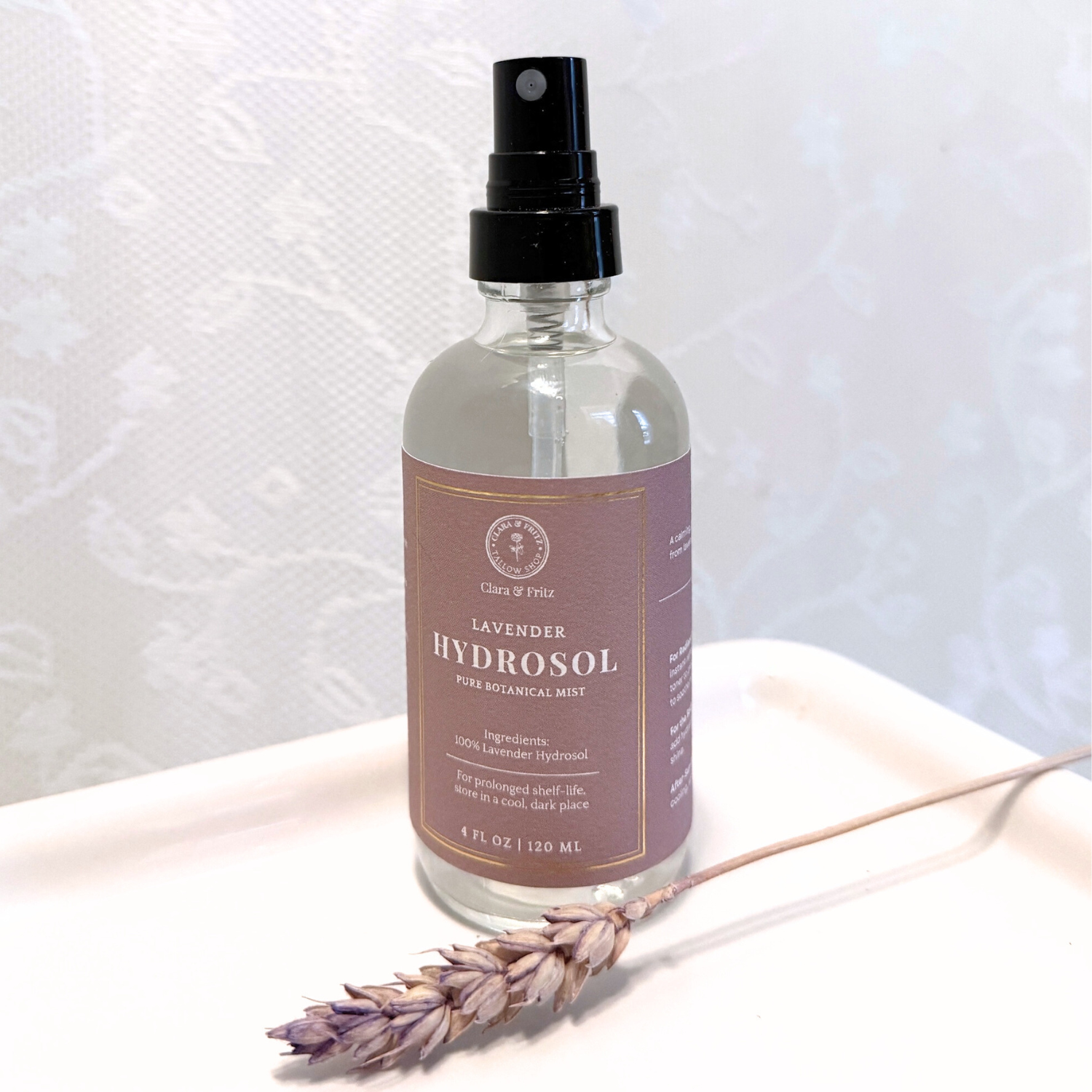 Glass bottle of Lavender Hydrosol for Facial Use with spray nozzle, next to a dried lavender sprig on a white tray
