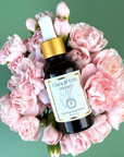 Serenity Calming Facial Serum surrounded by pink flowers on a green background