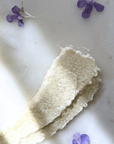 Pink Grapefruit Tallow Sugar Scrub with natural exfoliating texture, surrounded by purple flower petals on a light surface.