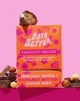 Date Better Snacks packaging with hazelnut praline and chocolate, featuring Medjool dates and hazelnut butter on a pink background.
