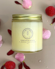 Essential Balm with Infused Calendula in a glass jar surrounded by pink petals and red berries on a beige surface.