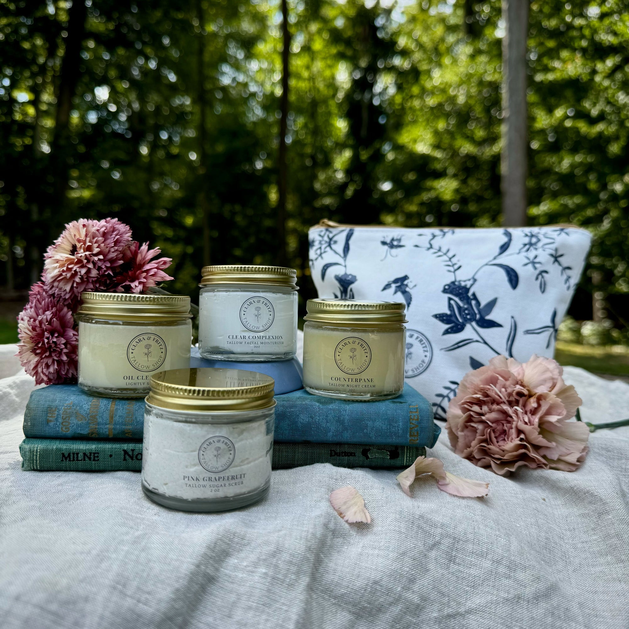 four jars and a bad near books and flowers on a linen cloth with trees in the background