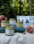 four jars and a bad near books and flowers on a linen cloth with trees in the background