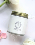Jar of scented whipped tallow balm with orange cream fragrance on a marble surface with flower petals.