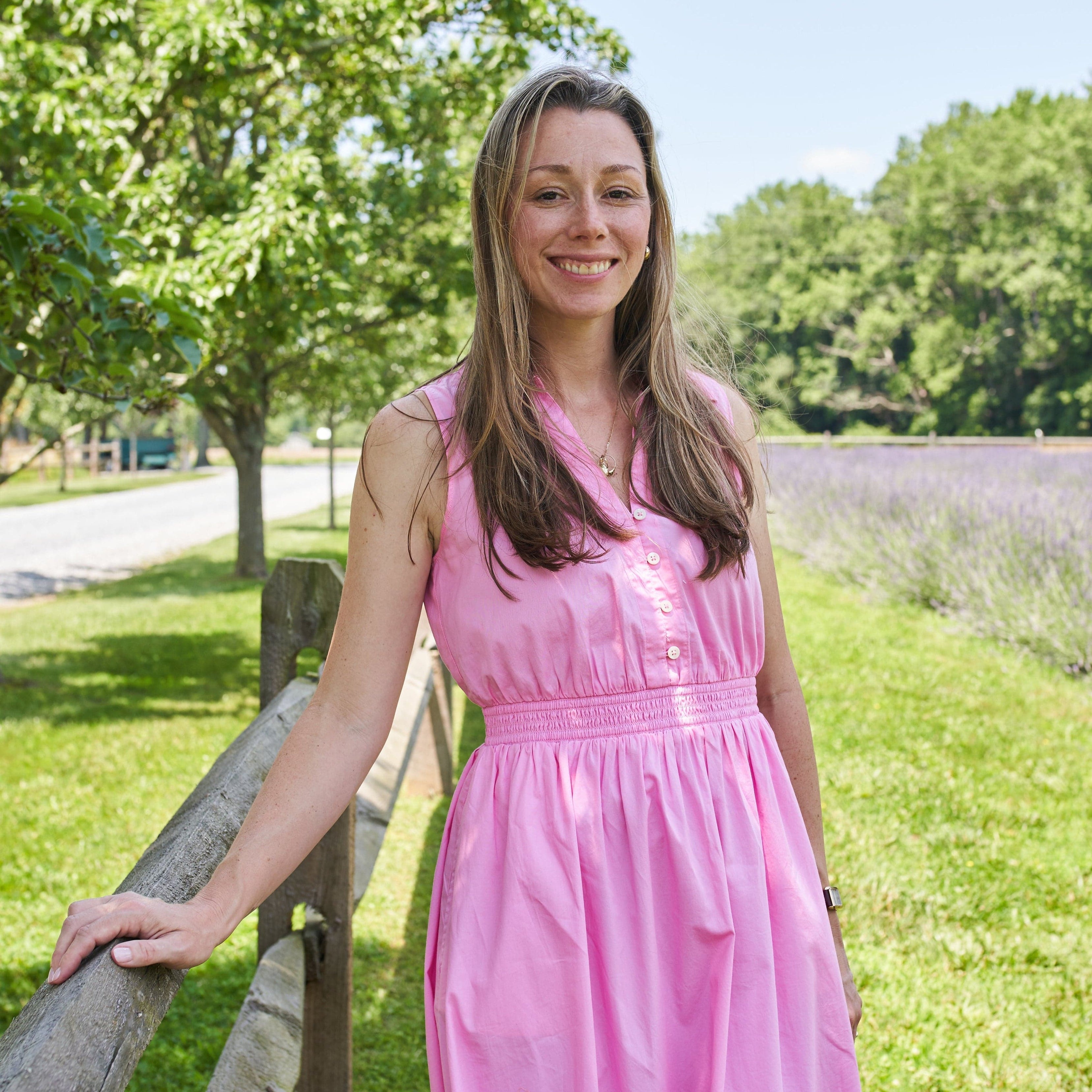 Woman in a pink dress standing outdoors with trees and a clear sky in the background